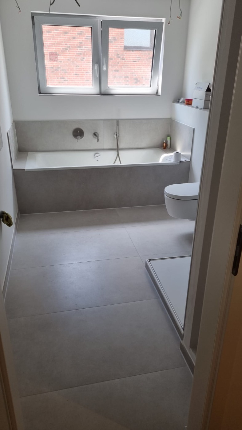 Saniertes Bad mit Wanne und grauen Fliesen