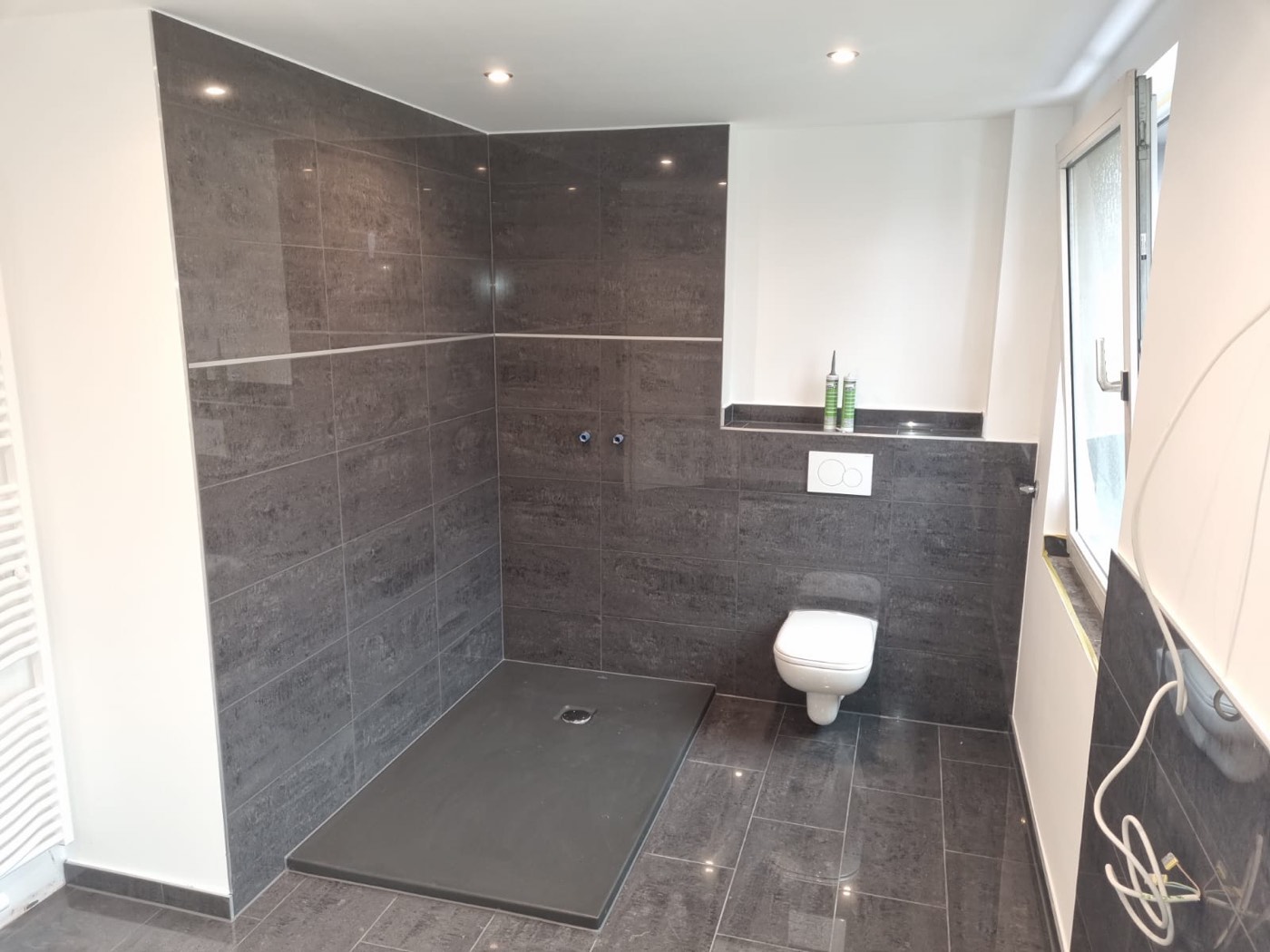 Fertig sanierte Walk-in-Dusche mit dunklen Fliesen